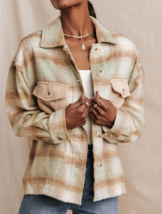 woman holding onto her plaid jacket. It's a brown, pink and green plaid jacket